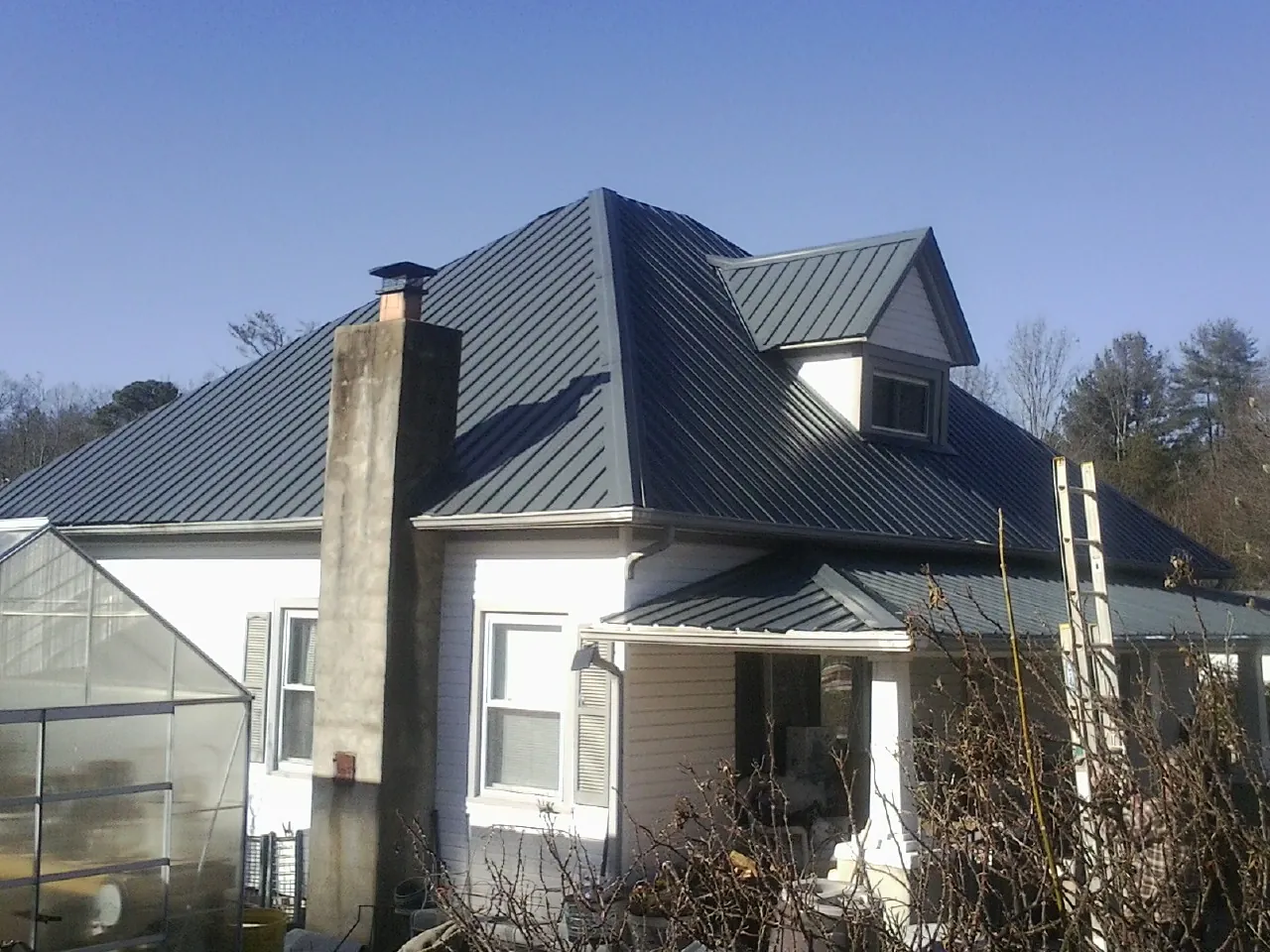 Dark blue standing seam metal roof on a white farmhouse with dormer in Peshastin