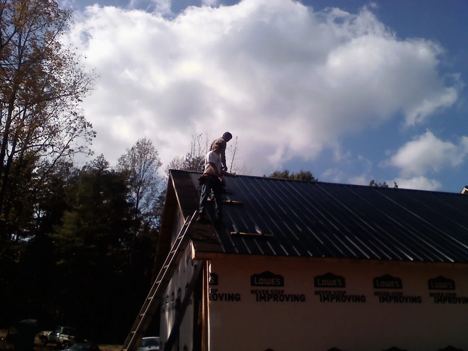 Roofer fastening dark metal panels high against a cloudy sky, from a Roof Inspection job in Peshastin