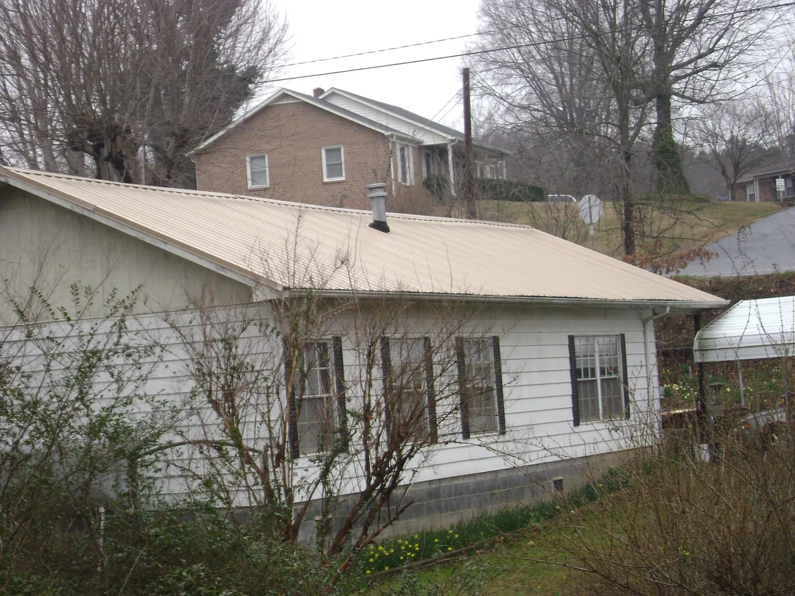 Tan metal roof on a white sided house set into a hillside — Commercial Roofing by Roofing Brothers in Peshastin